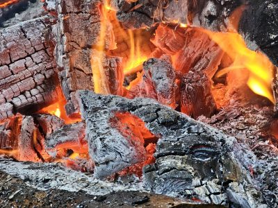 Orange flames lick the dark, red heat on the wood, ash turns into smoke