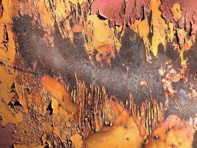 Orange paint breaks off, dark rust waits beneath the skin, yellow edges curl