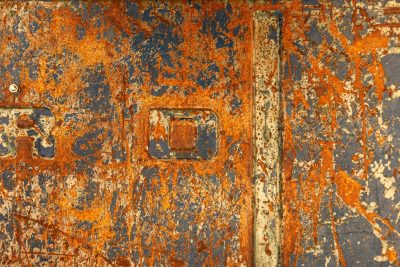 Orange rust blooms bright, heavy scars on fading blue, letters slowly fade