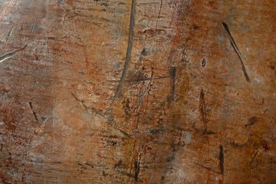 Orange rust eats the blue car steel, heavy scales mark the body, grit holds the decay