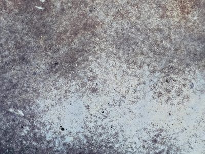 Pale blue paint recedes, rust consumes the metal sheet, cracked patterns emerge