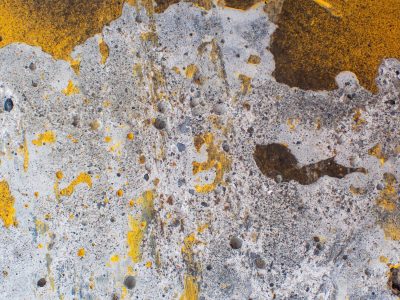 Yellow paint splatters, rough grey concrete wears away, pitted stone remains