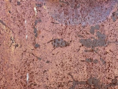 Pink rust coats the steel, dark scars break the fading red, time leaves heavy grit
