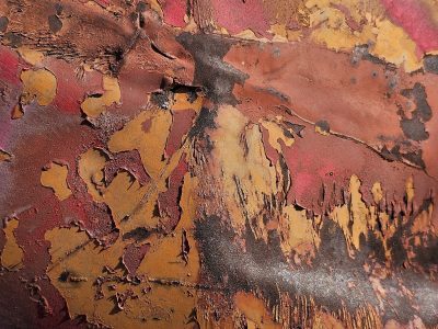 Red paint fades to brown, heavy rust eats the steel plate, grit claims the surface