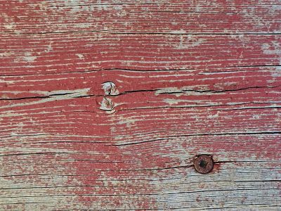 Red paint peels away, knots and cracks trace the old grain, iron holds the wood.