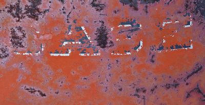 Red rust eats the sign, white paint peels from pitted steel, letters fade away