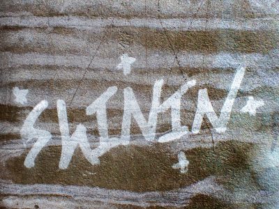 Silver paint on stone, bright flakes meet the grey grit, light catches the skin