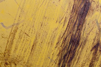 Bright yellow face fades, rust bleeds in long dark streaks, steel shows age in scars