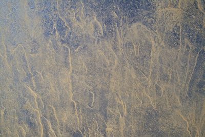 Silver skin has pits, jagged lines trace the metal, light catches the grit