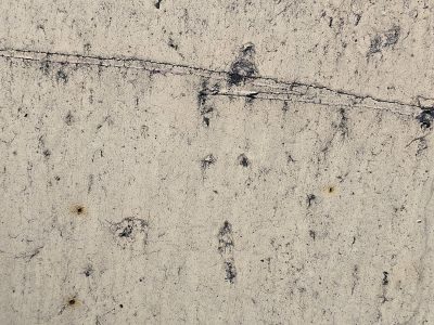 Tan pits on the wall, black streaks mark the fading paint, grit meets the rough board