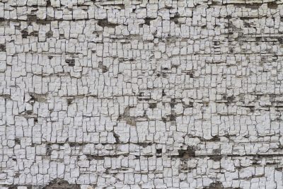 White paint peels away, brown wood waits beneath the cracks, grit holds the surface
