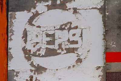 White paint peels away, red and orange line the edge, weather claims the sign