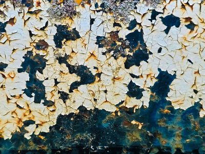 White scales peel from steel, lichen blooms on rusted dark, time creates the art.