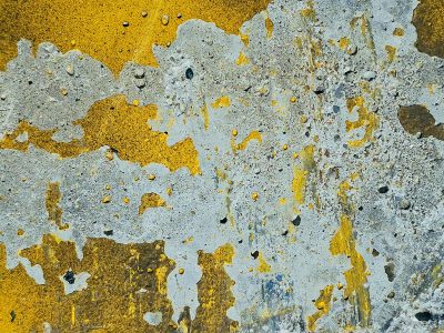 Yellow paint peels back, grey concrete holds the surface, time wears down the line.