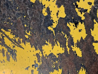 Yellow skin peels back, dark rust blooms on heavy steel, grit marks the surface