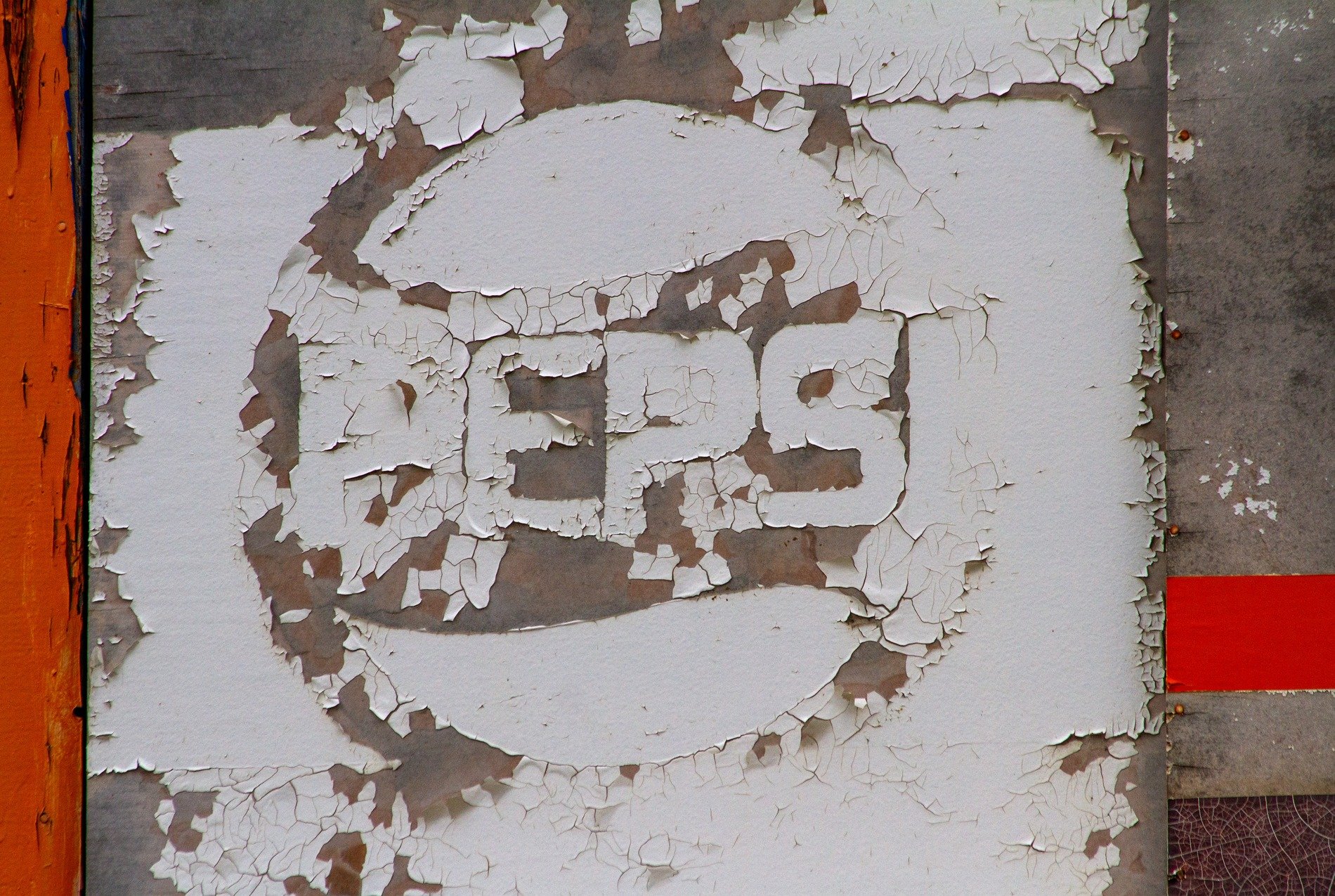 White paint peels away, red and orange line the edge, weather claims the sign