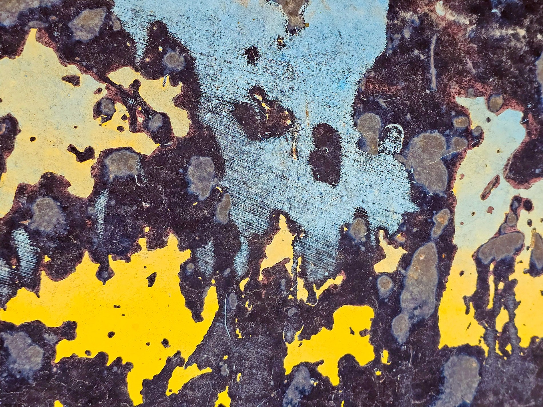 Yellow flakes away, black and blue hide underneath, metal shows its scars.