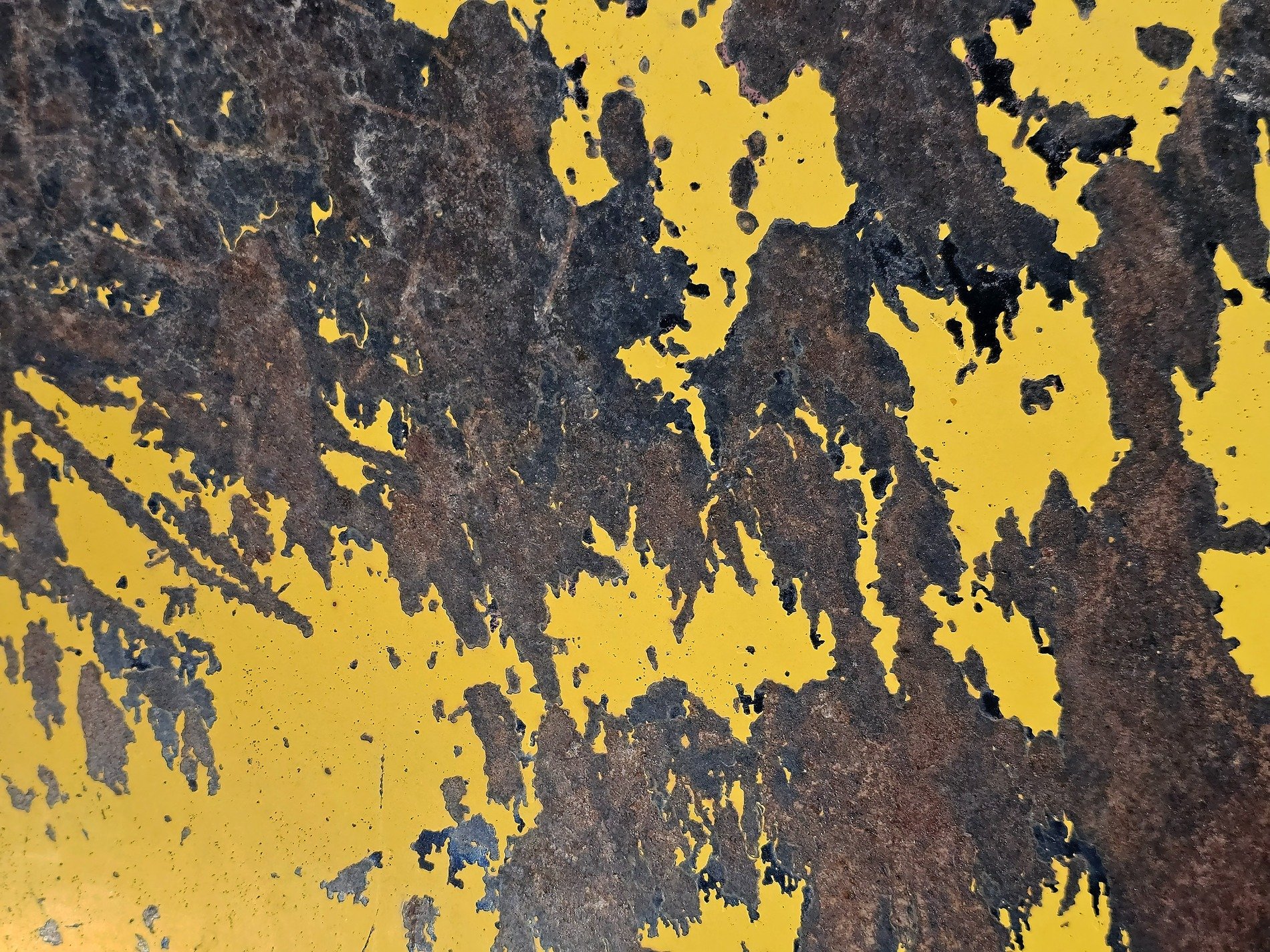 Yellow skin peels back, dark rust blooms on heavy steel, grit marks the surface