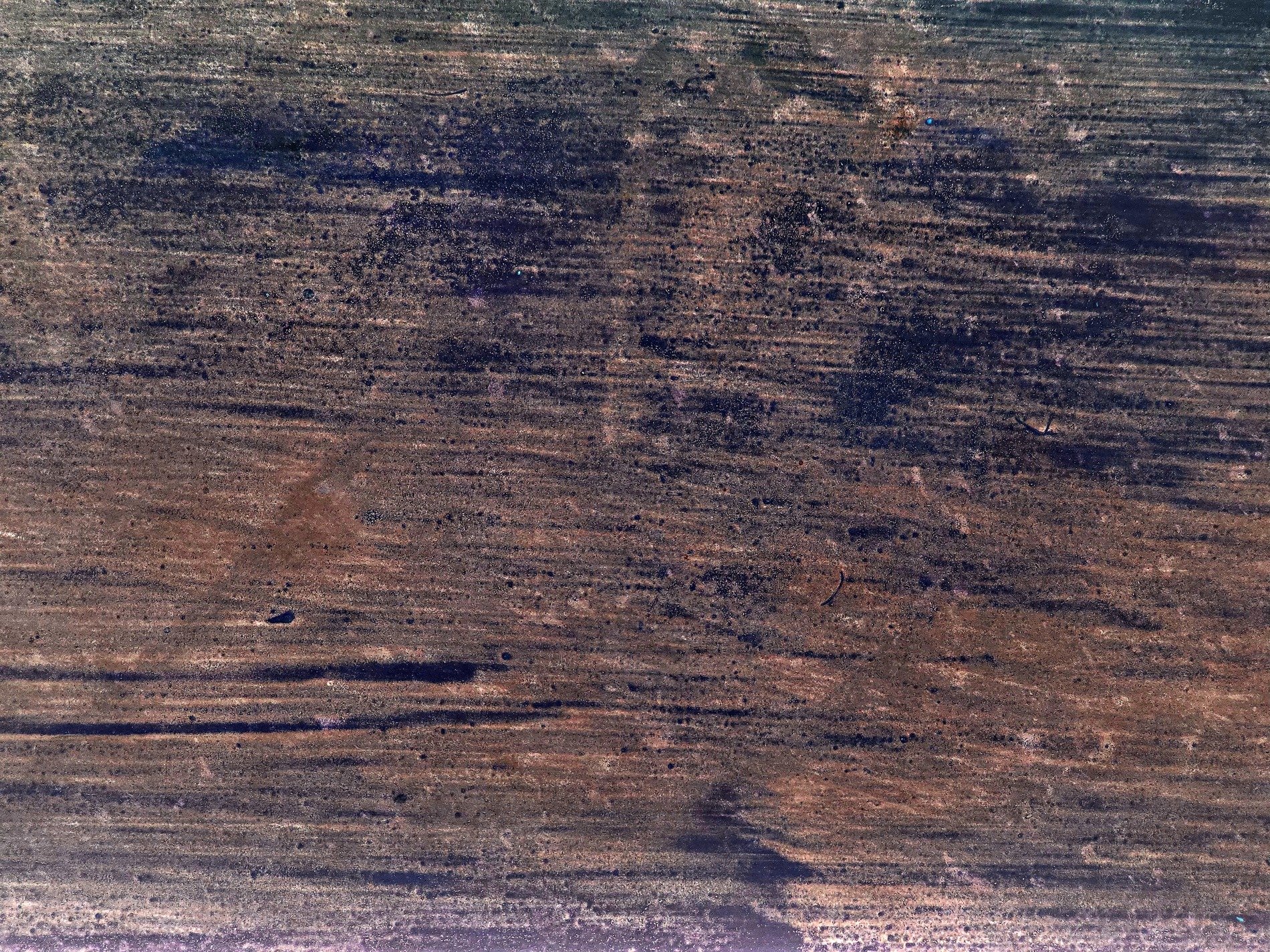 Burnt grain wears the dust, dark stains line the weathered face, time marks every ridge