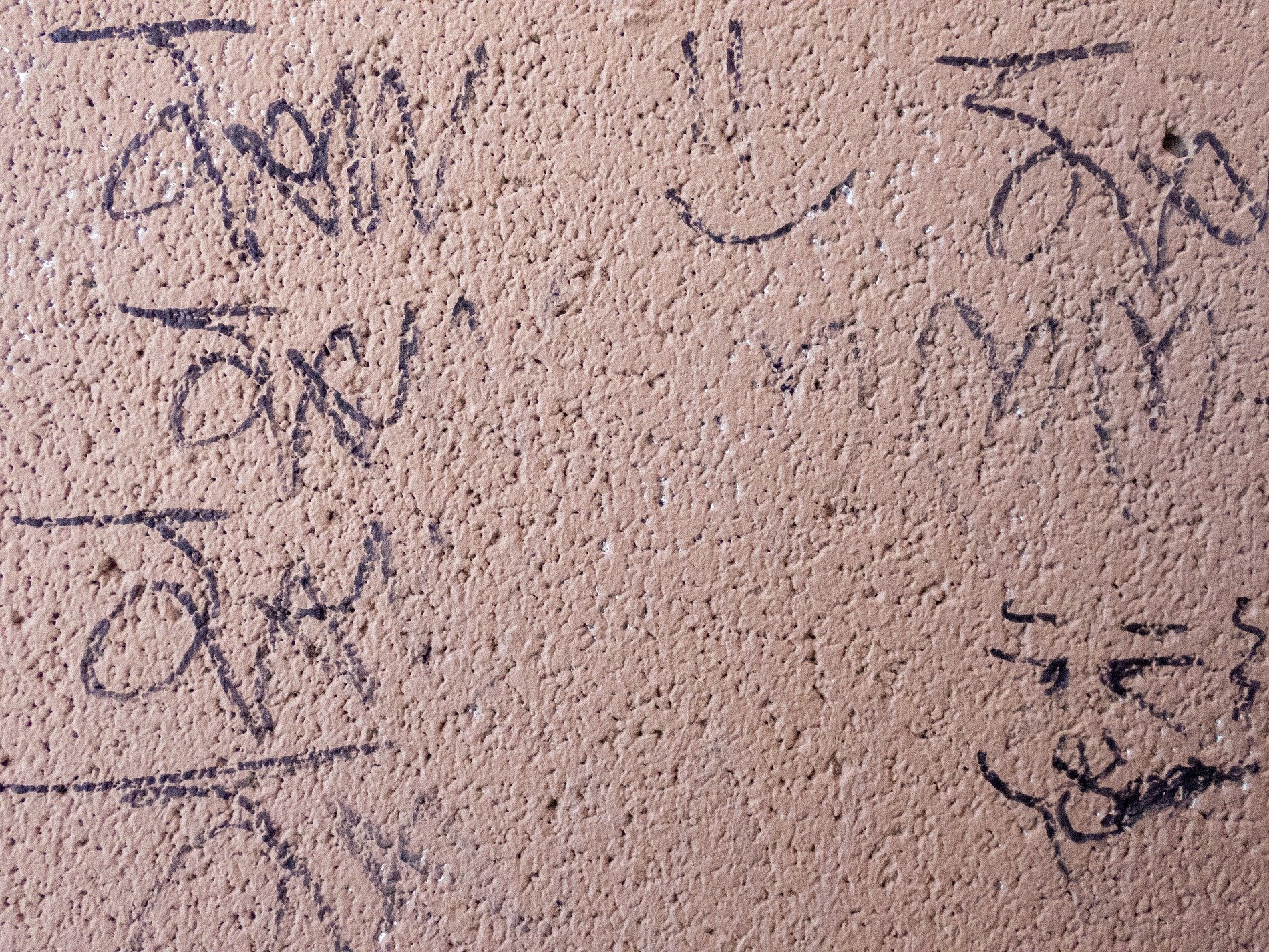 Black ink on the wall, rough stone holds a hidden face, fading marks remain