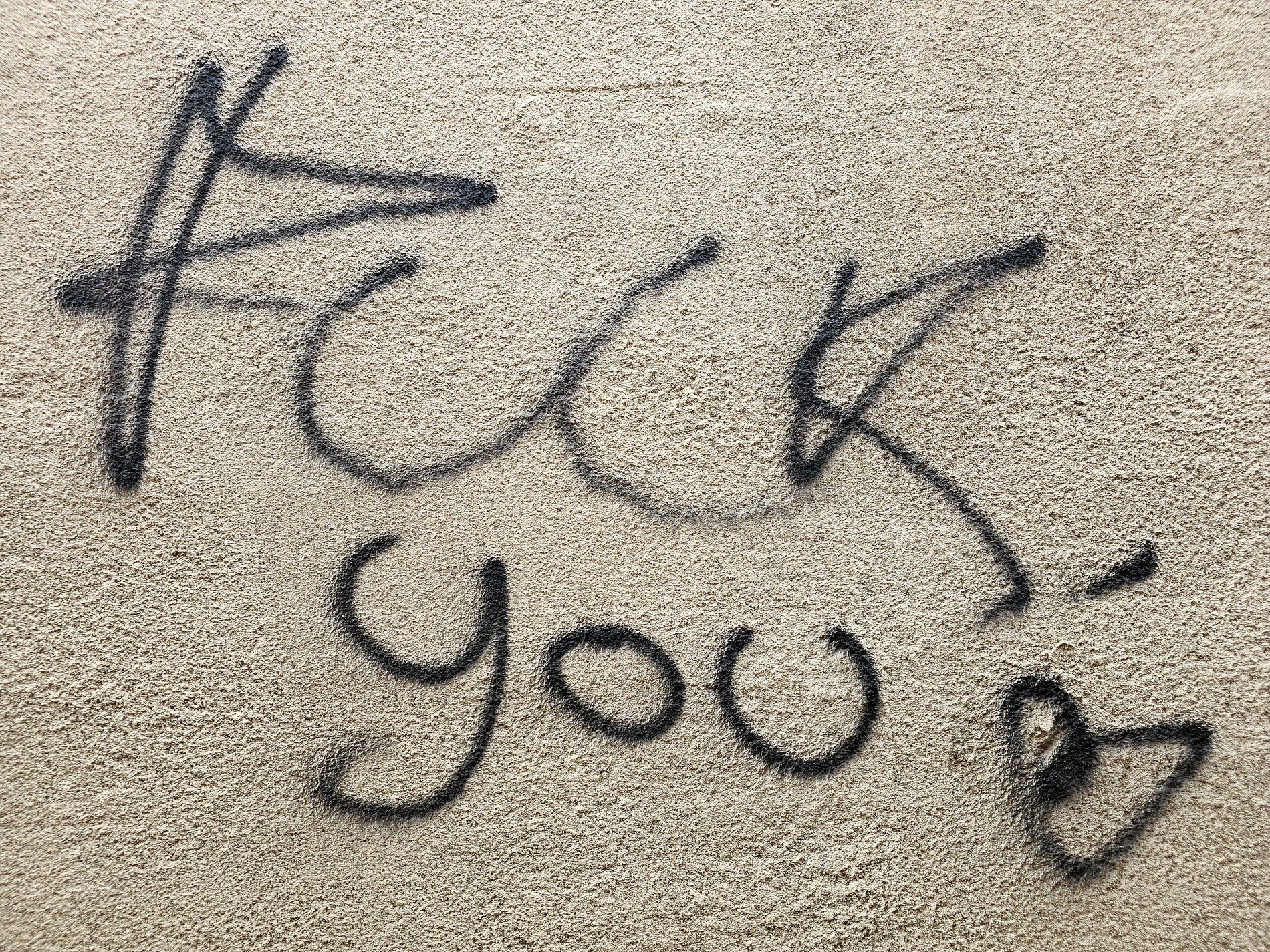 Black paint on the wall, harsh words flow in cursive script, small heart ends the tag