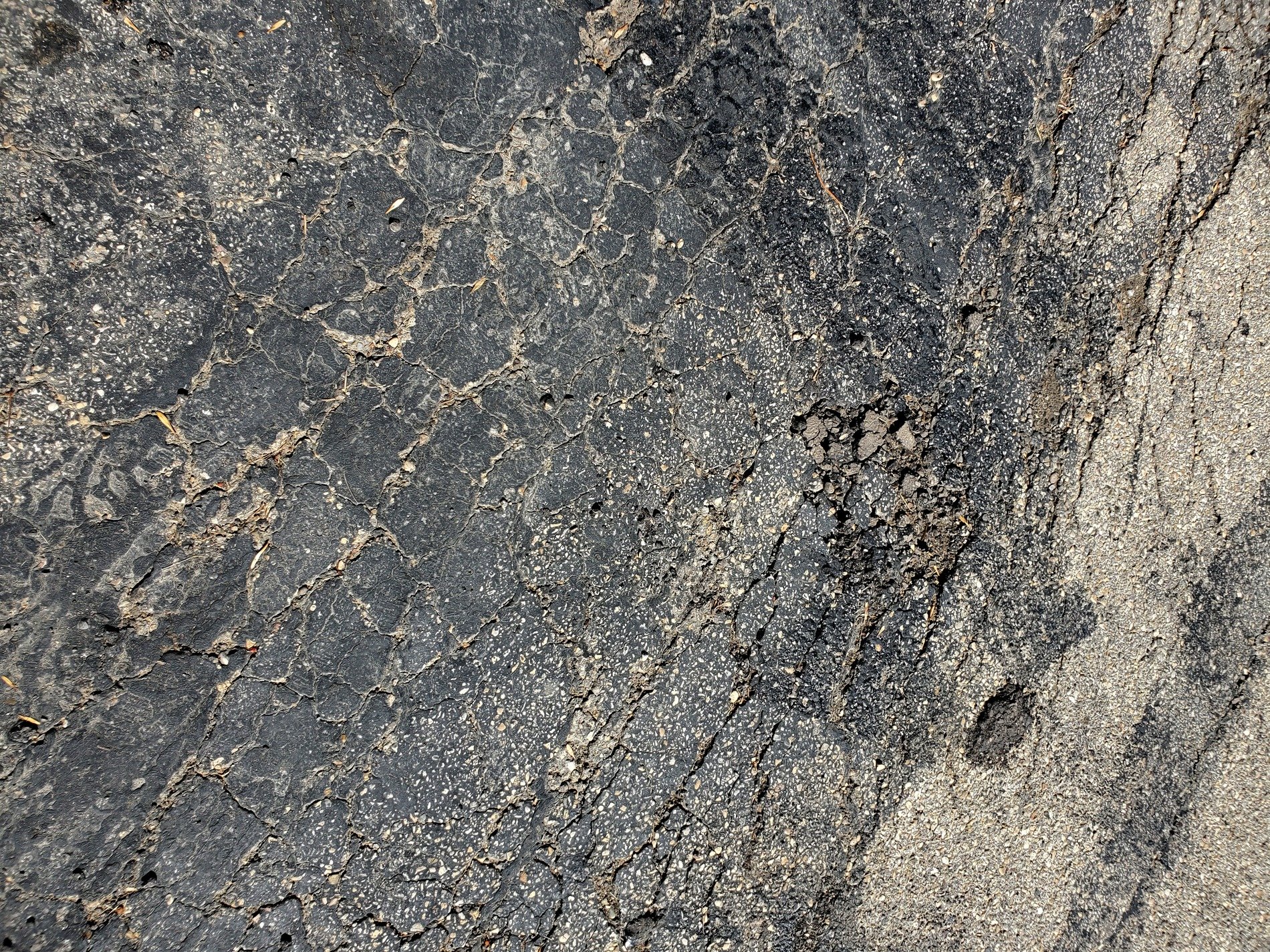 Black road starts to break, spider webs of tiny cracks, sun bleaches the stone