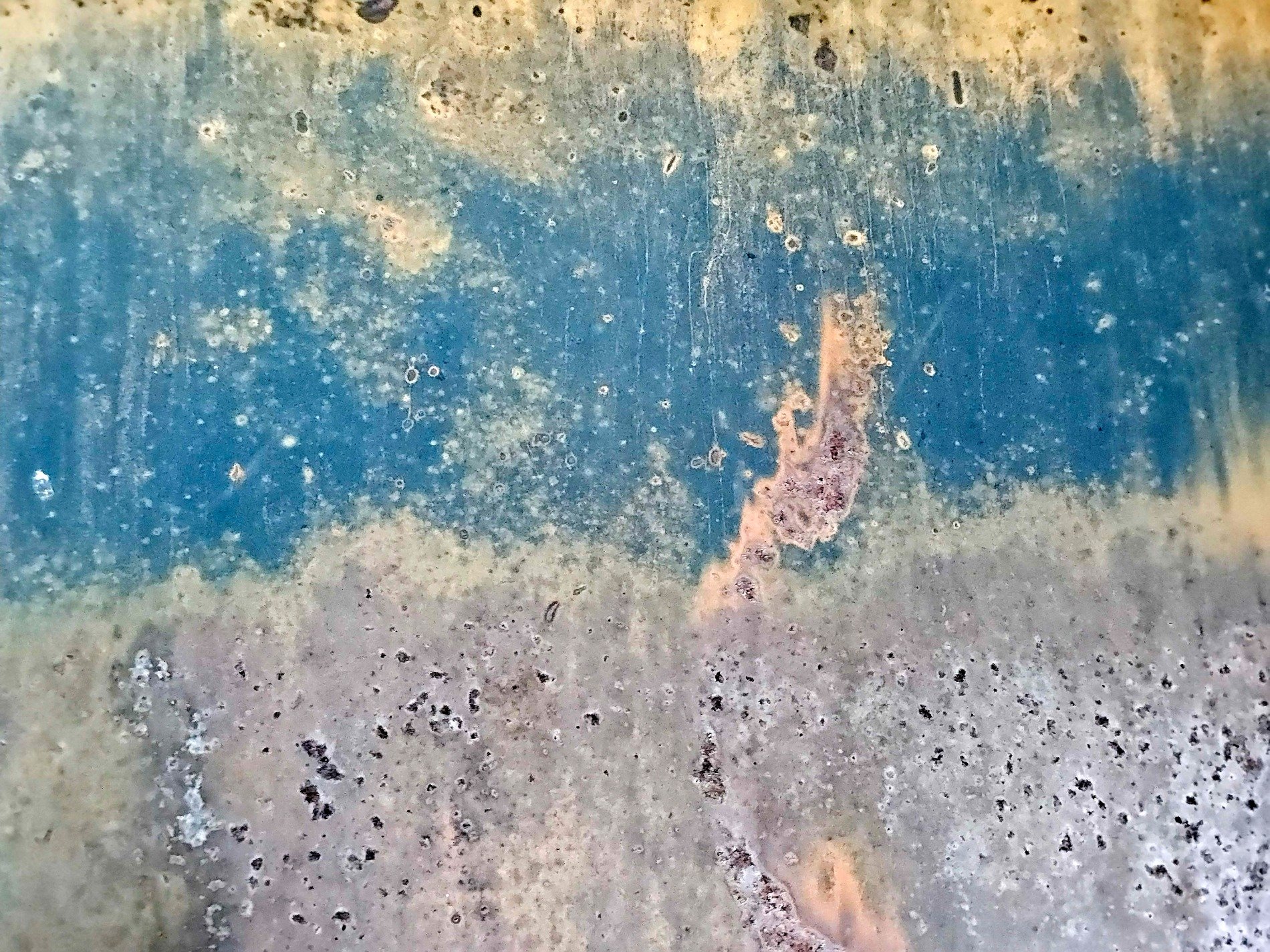 Blue band wears away, pitted metal meets the light, rust blooms in the gaps