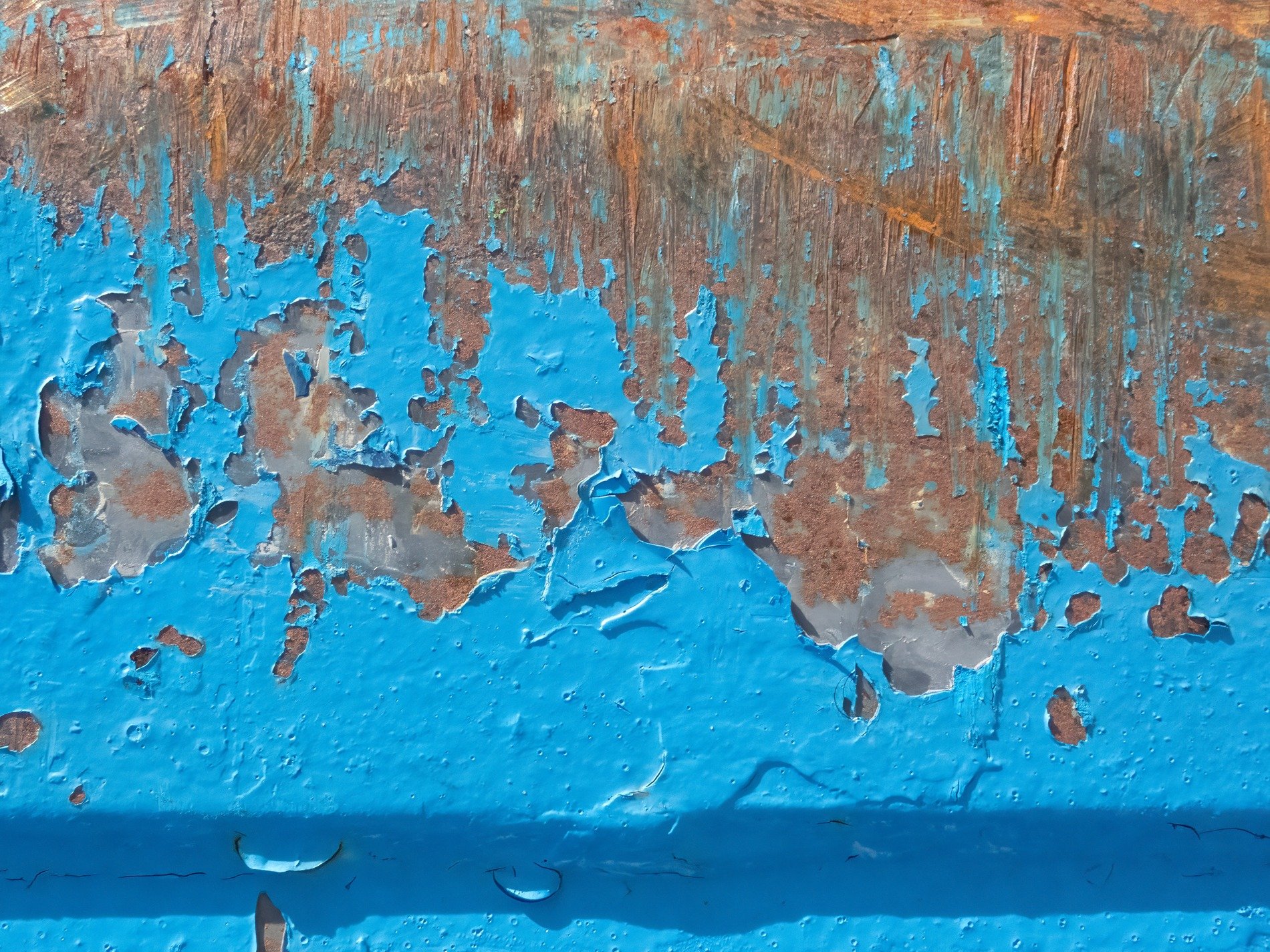 Blue flakes peel away, rust blooms on the iron skin, time chips at the paint