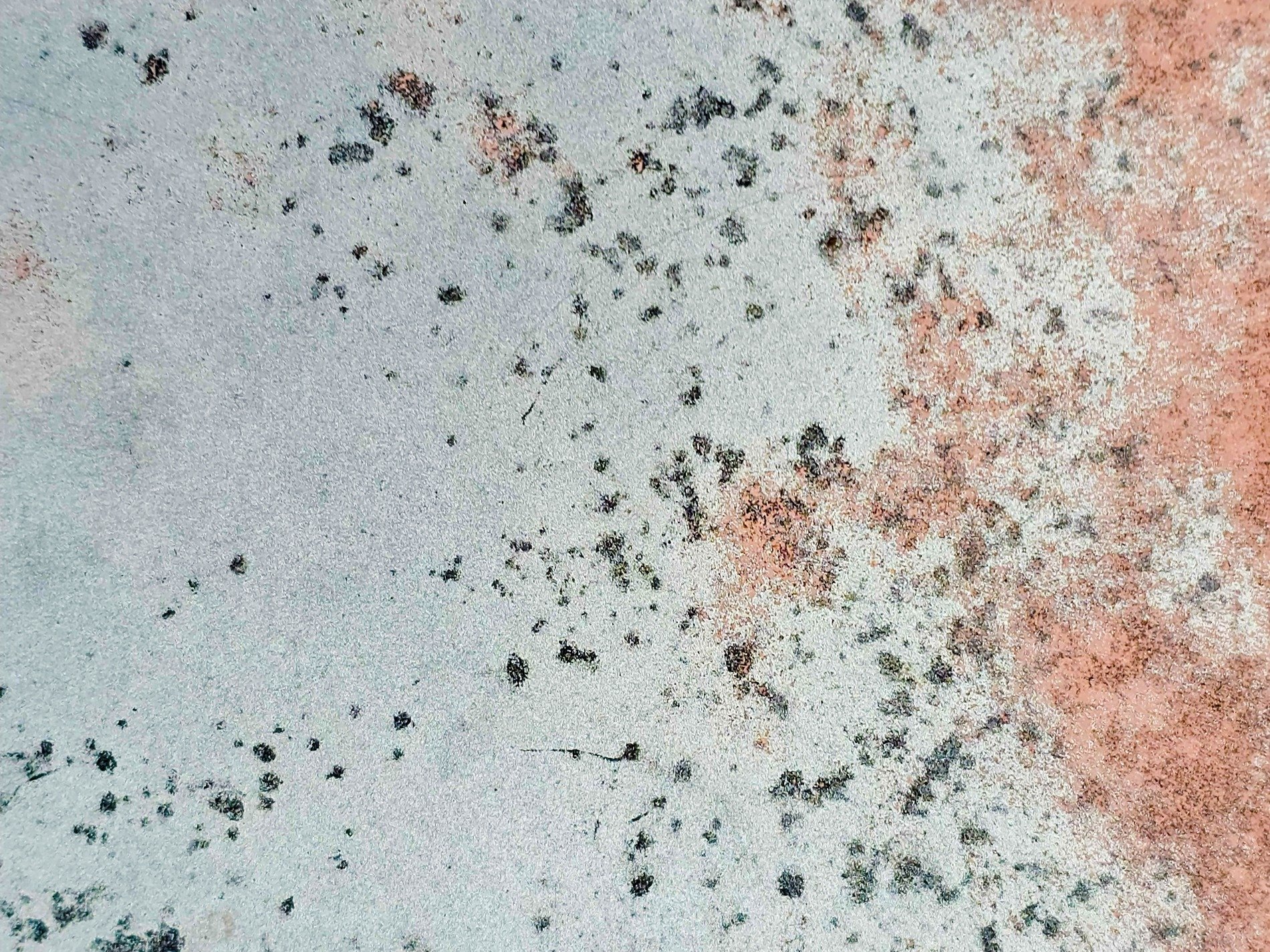 Pale blue surface fades, copper rust creeps from the edge, dark spots mark the age