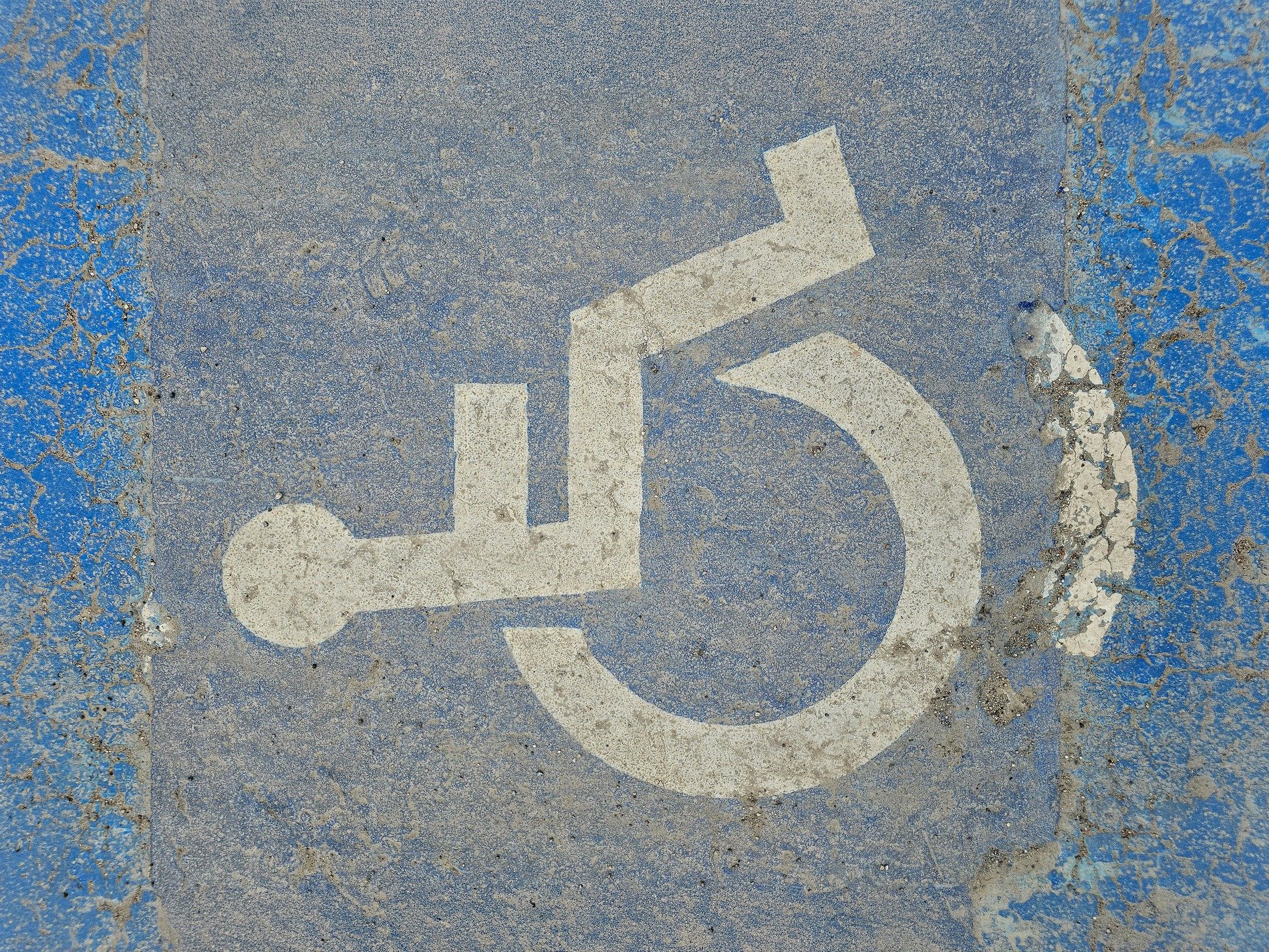 Blue paint chips away, white symbol marks the pavement, stone shows through the cracks