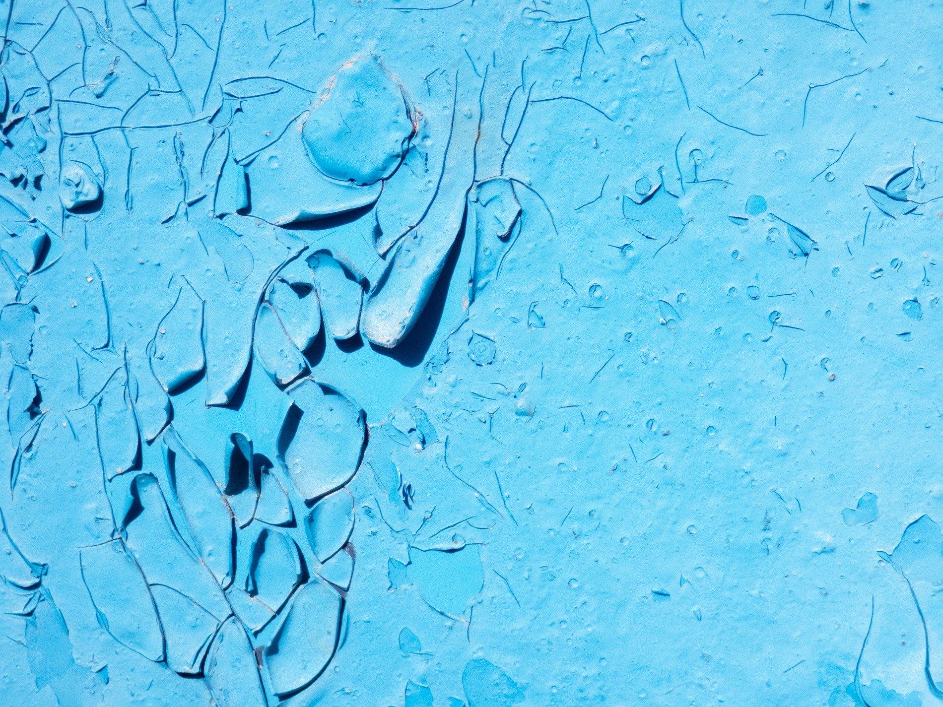 Blue paint curls away, deep cracks map the aged surface, shadows fall on chips