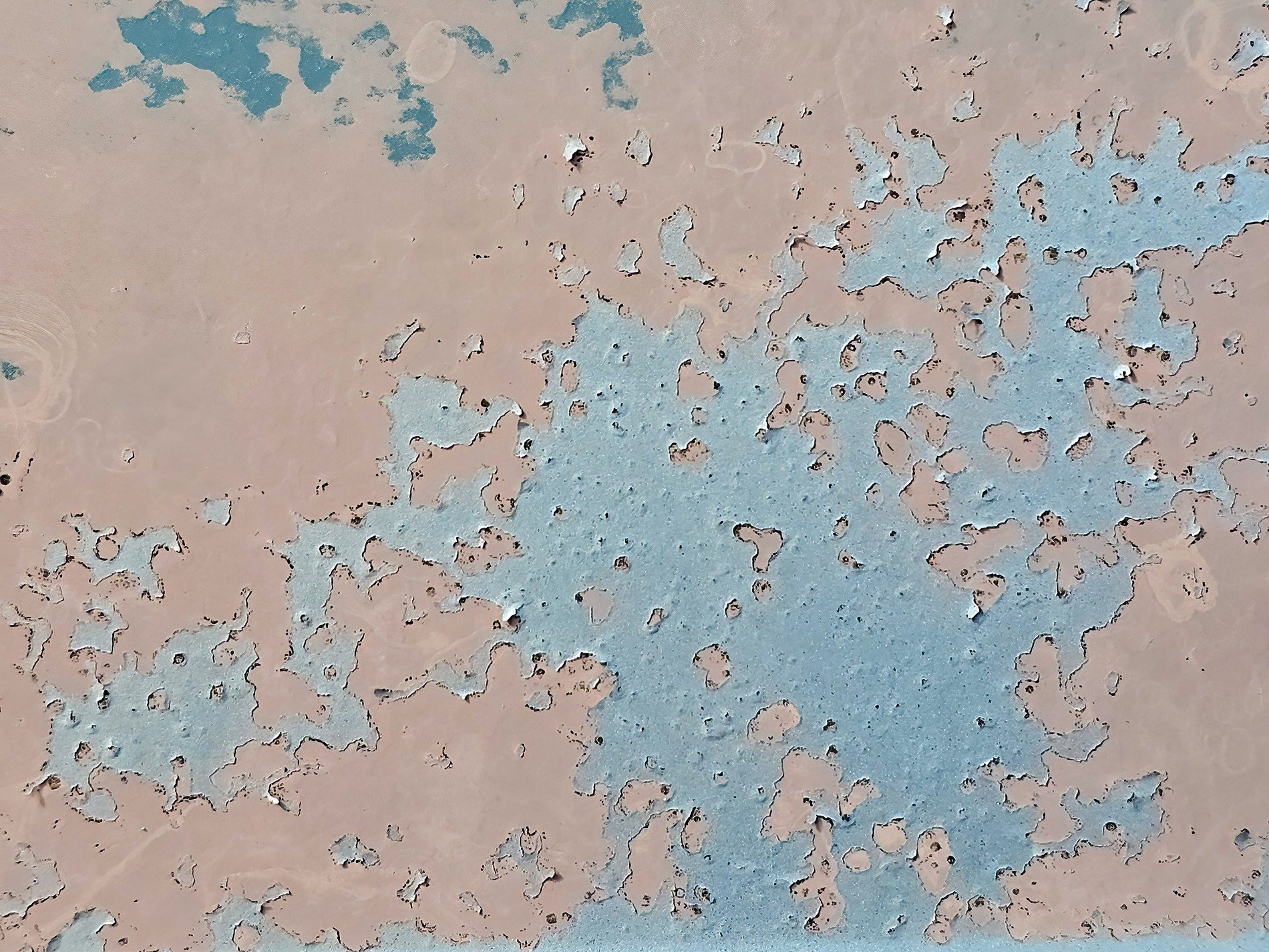 Blue paint curls away, tan metal hides underneath, time peels back the layers