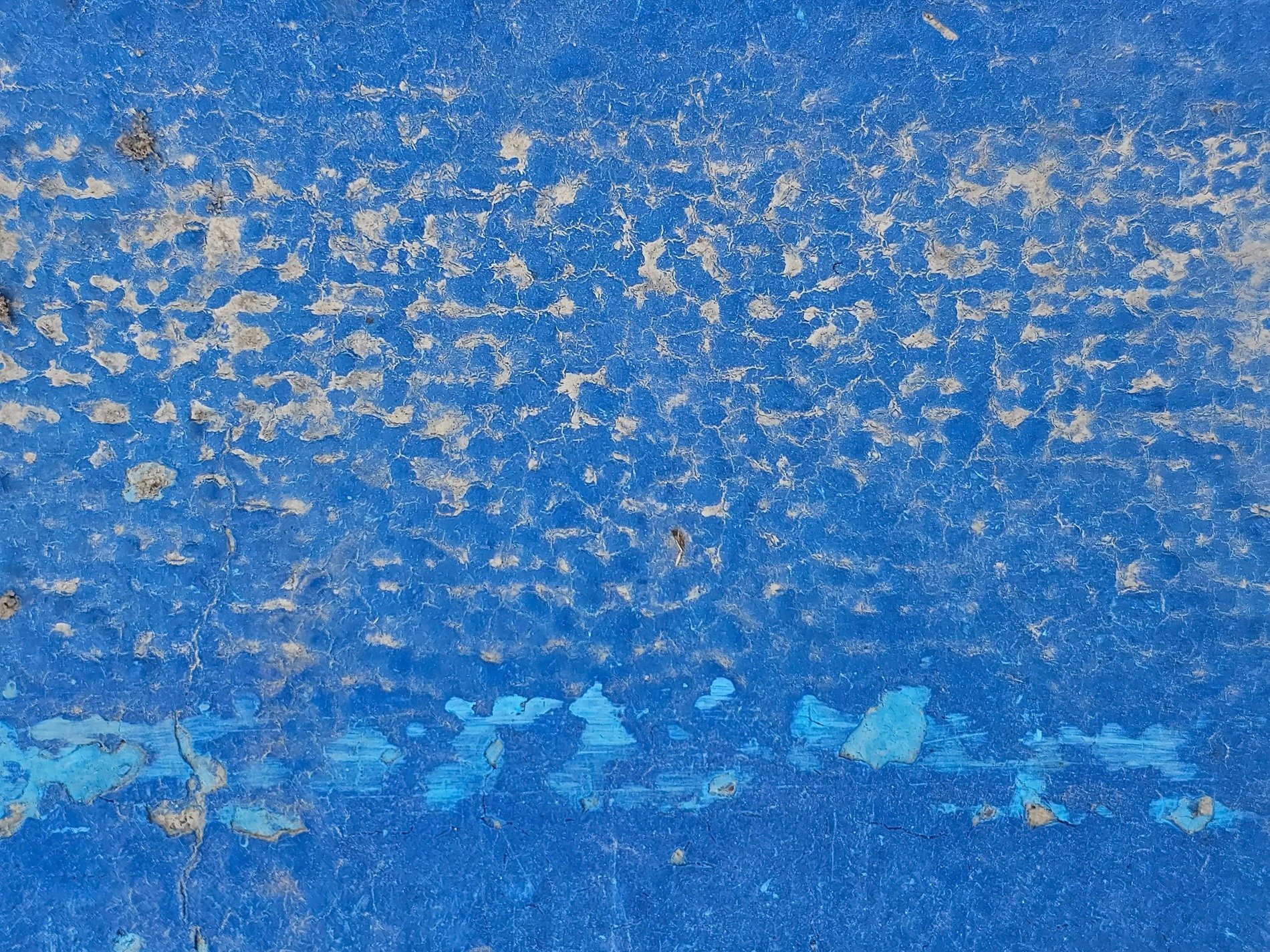 Blue paint peels away, grey cracks trace the weathered skin, deep scars mark the ground