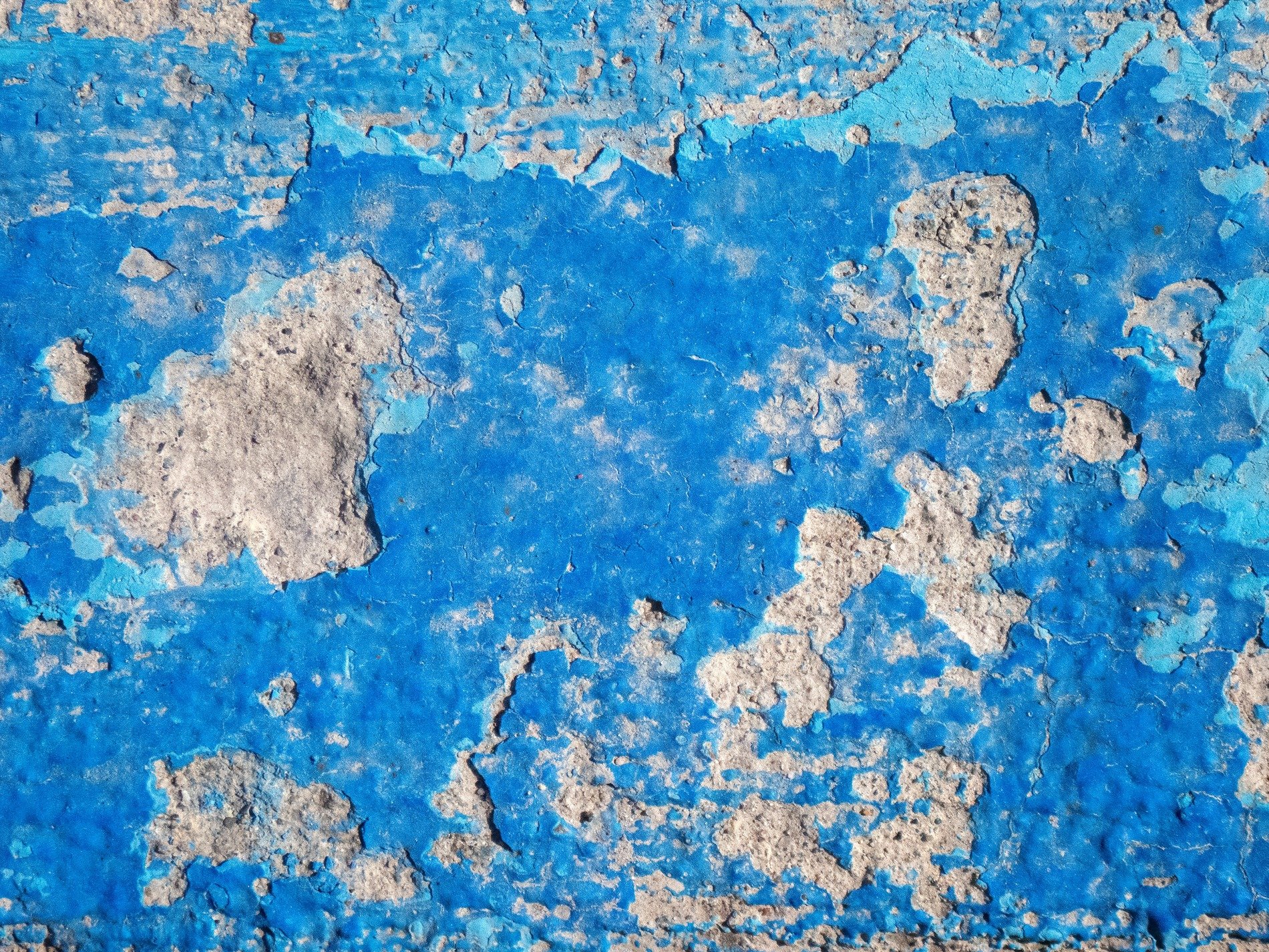 Blue paint starts to peel, rough grey concrete hides beneath, time wears down the skin