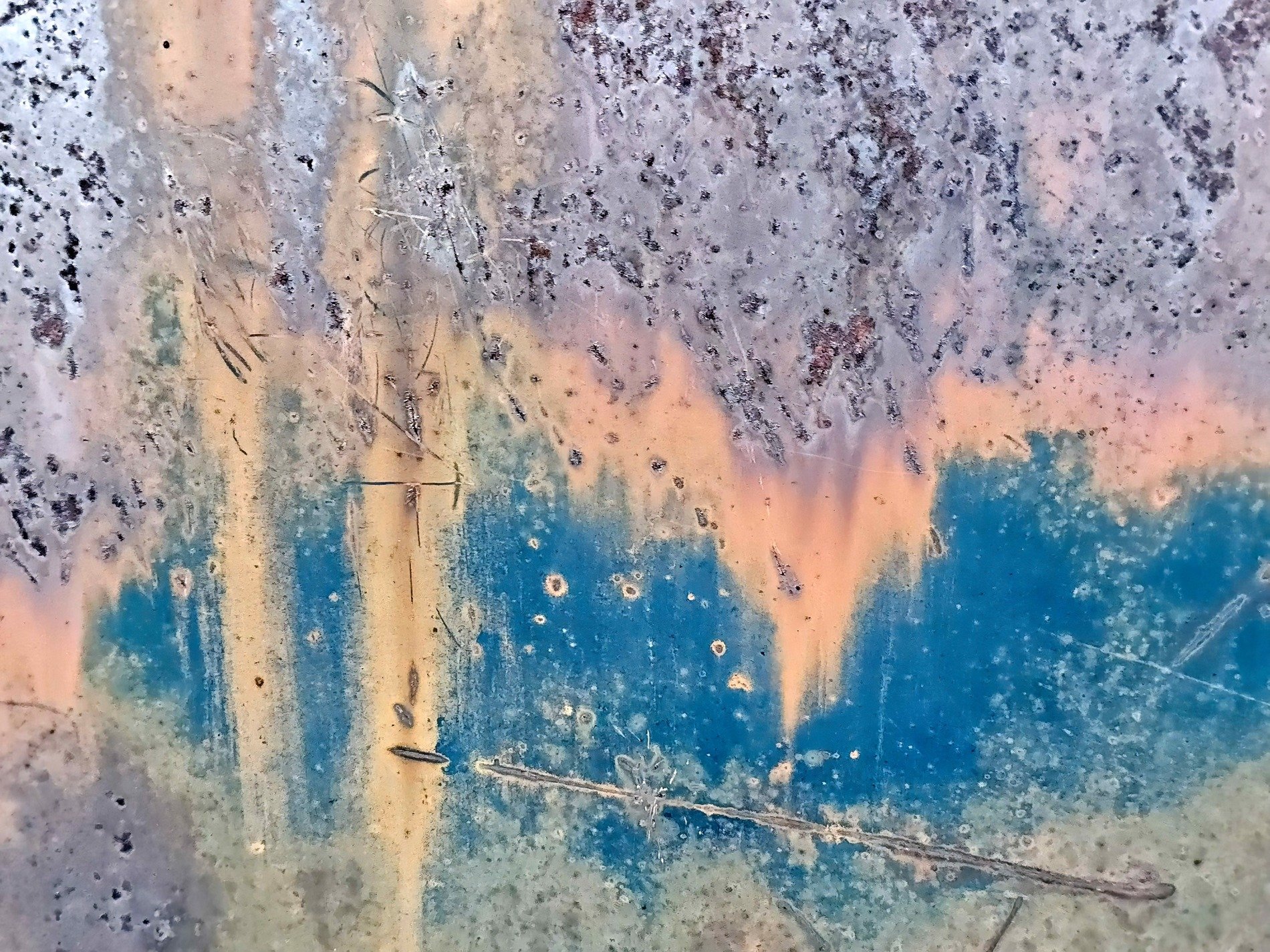 Blue paint wears away, orange rust bleeds through the steel, silver pits remain
