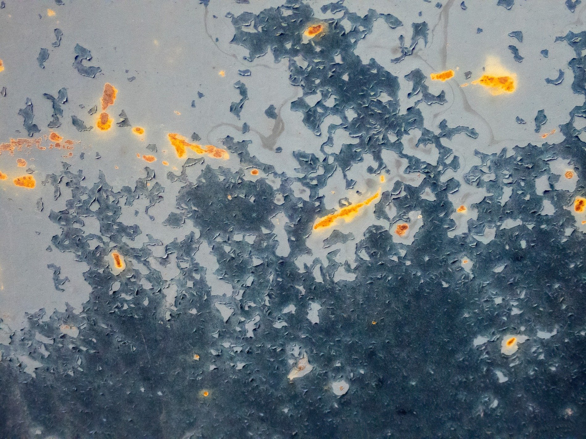 Blue skin has rust spots, jagged paths trace the surface, light catches the grit