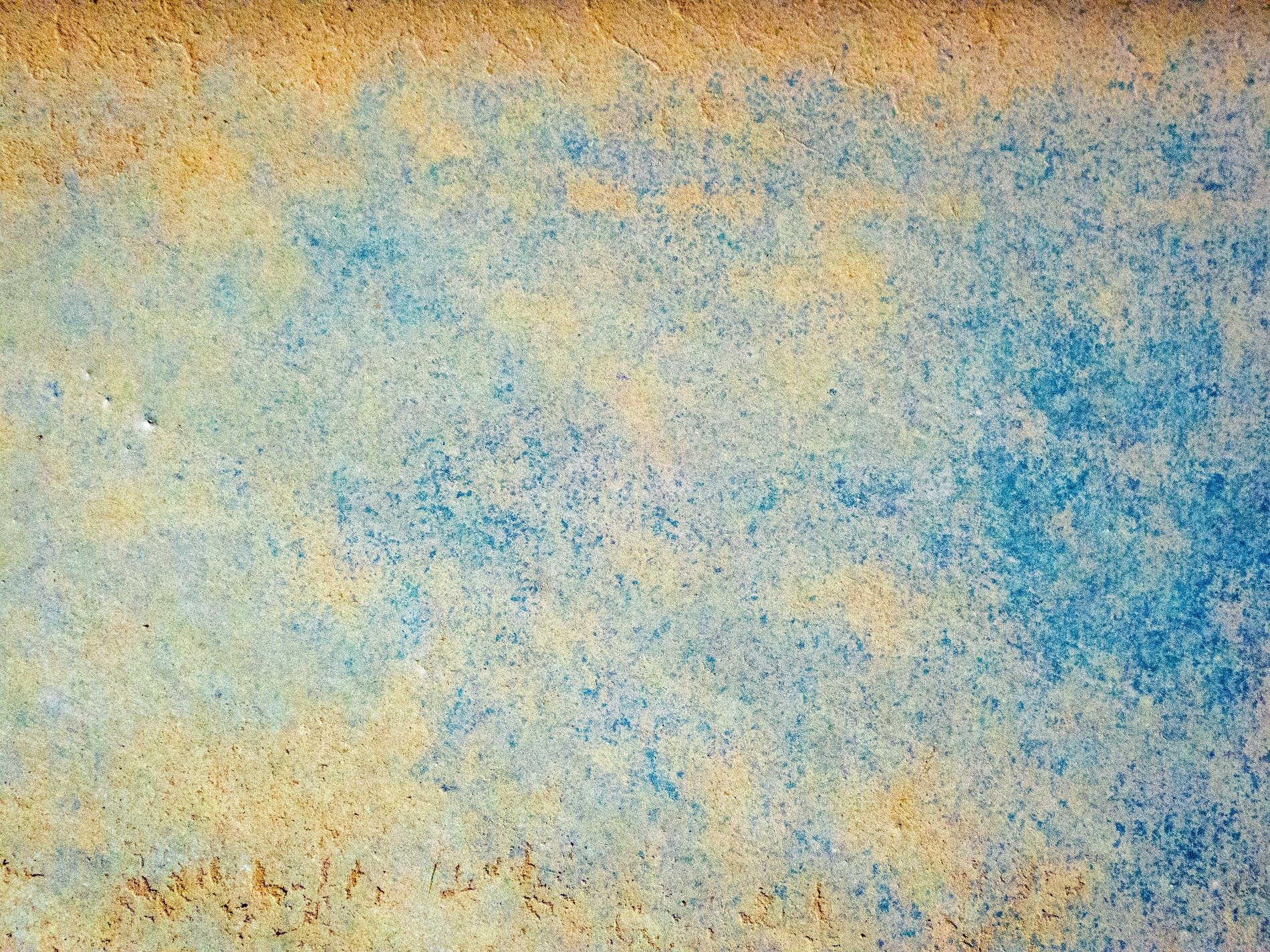 Blue wash fades away, golden sand beneath the sea, weathered stone remains