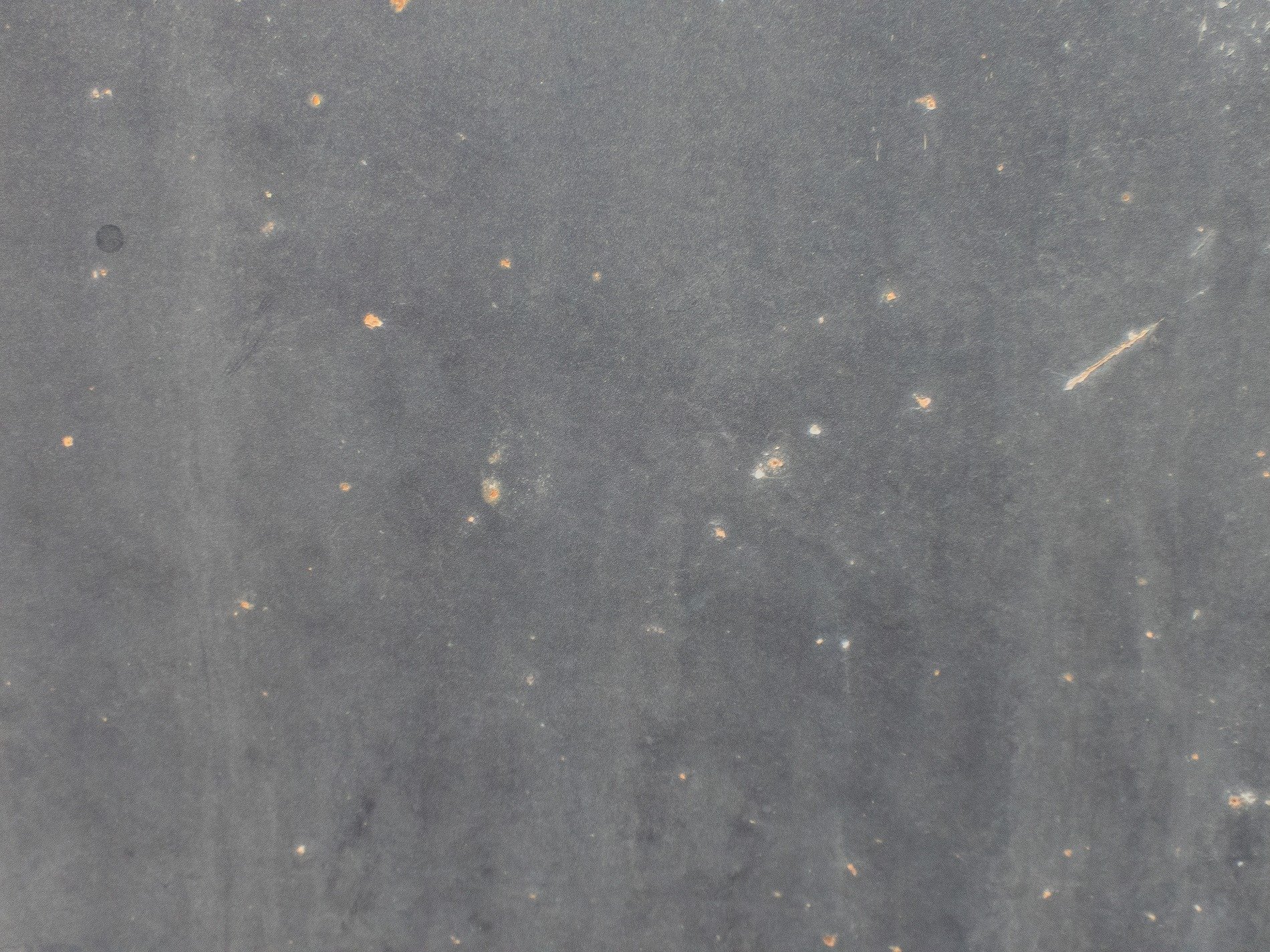 Charcoal metal skin, orange rust blooms like small stars, steel awaits the rain