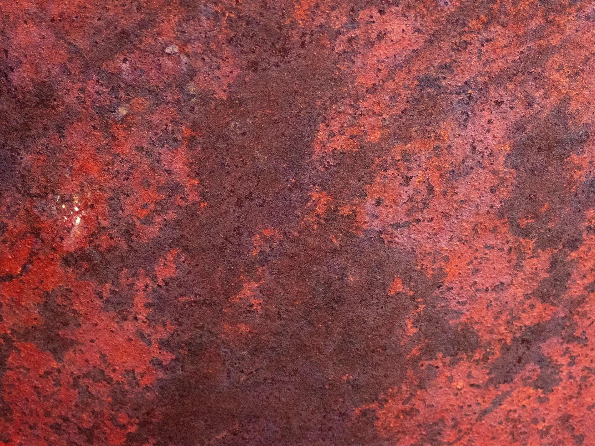 Crimson oxide spreads, pitted metal holds the heat, iron flakes away