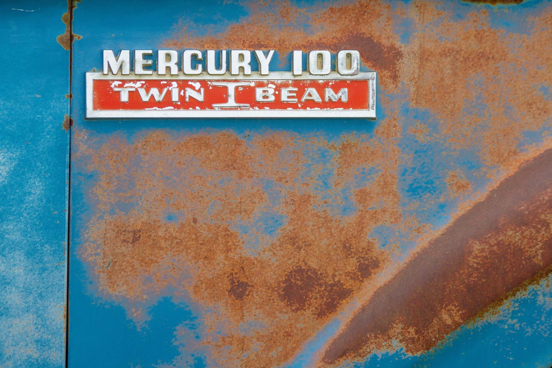 Faded blue surface, orange rust eats through the steel, vintage badge remains