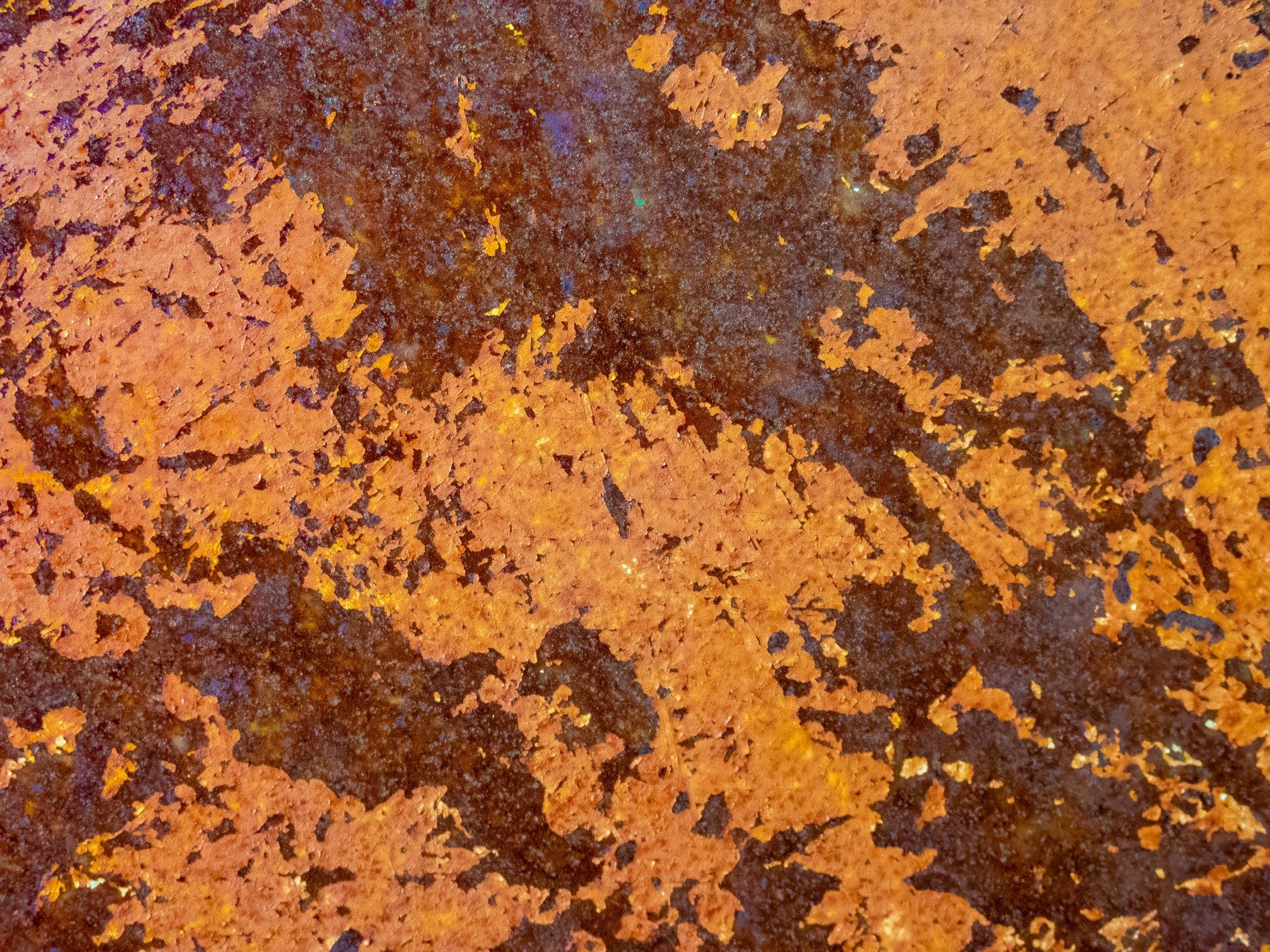 Flaked iron spreads out, dark shadows bleed through the crust, oxidation blooms