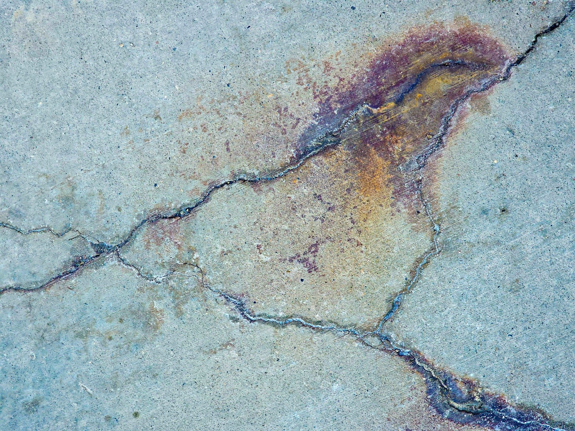 Gray stone splits apart, orange stain bleeds from the crack, weathered ground remains