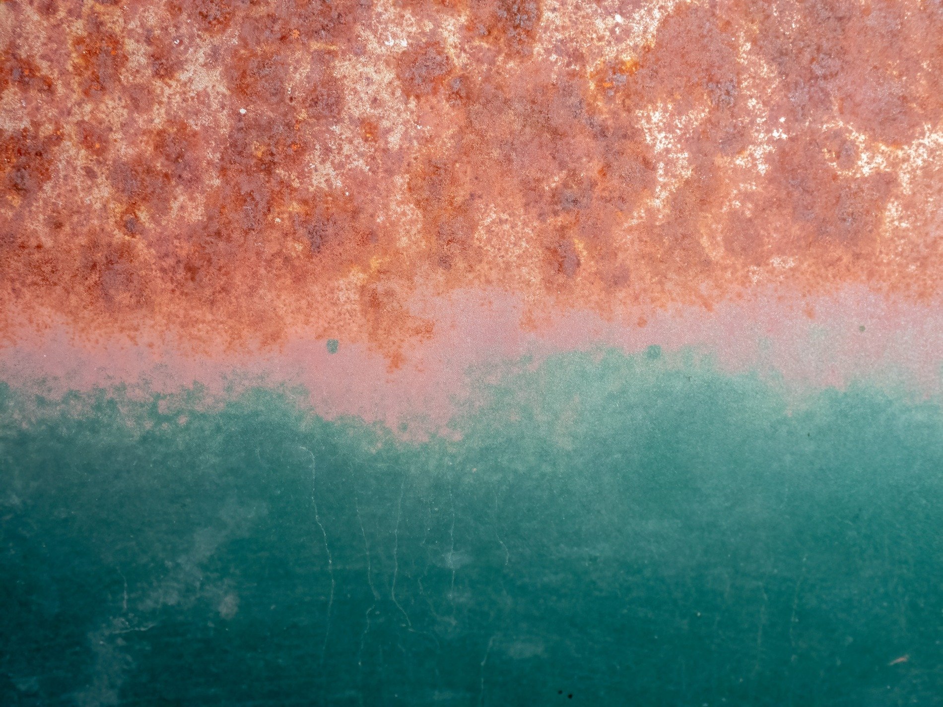 Orange rust creeps down, teal paint holds the line against, time eats through the steel