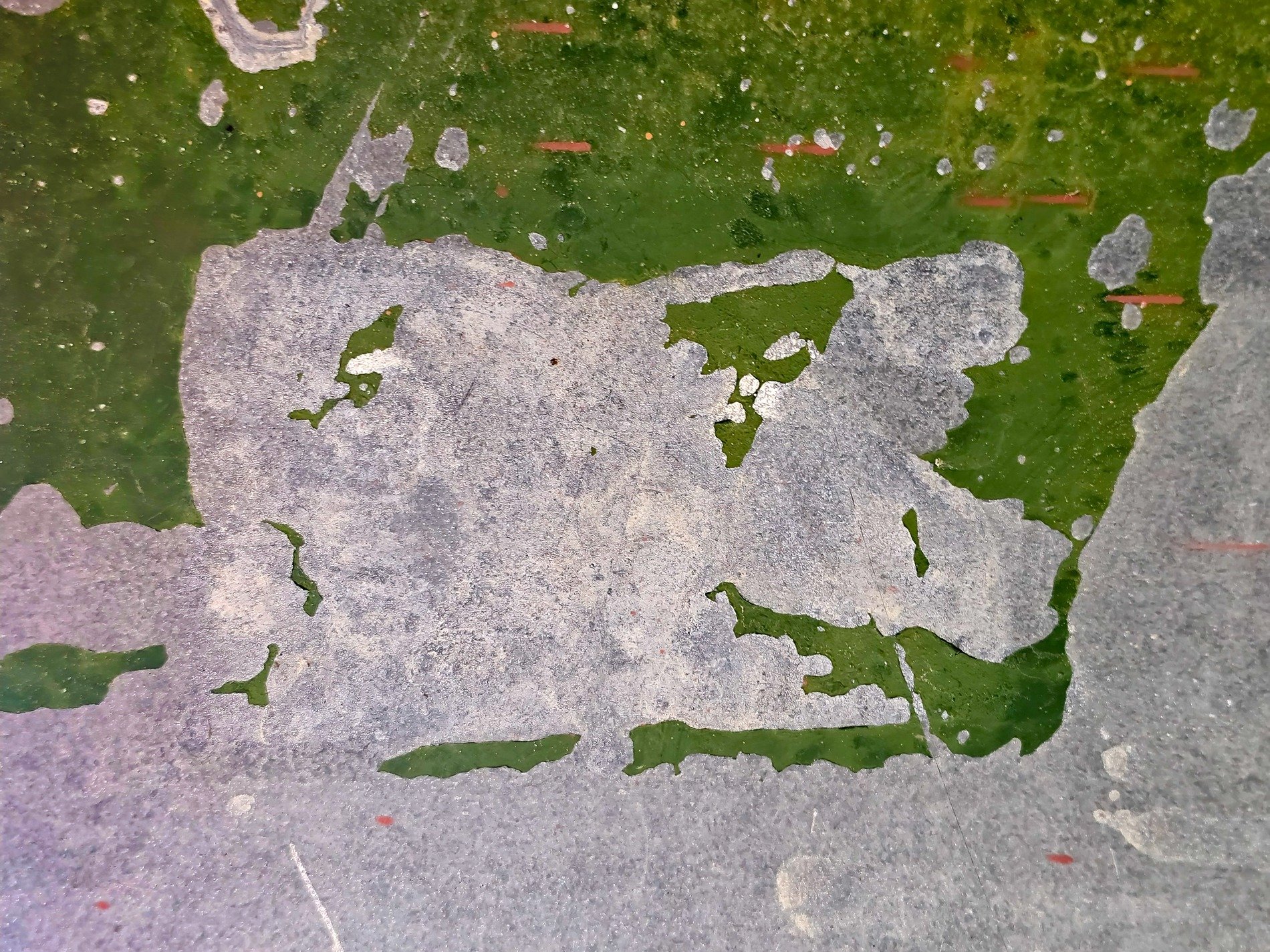 Green paint flakes away, gray stone surface is revealed, layers of decay