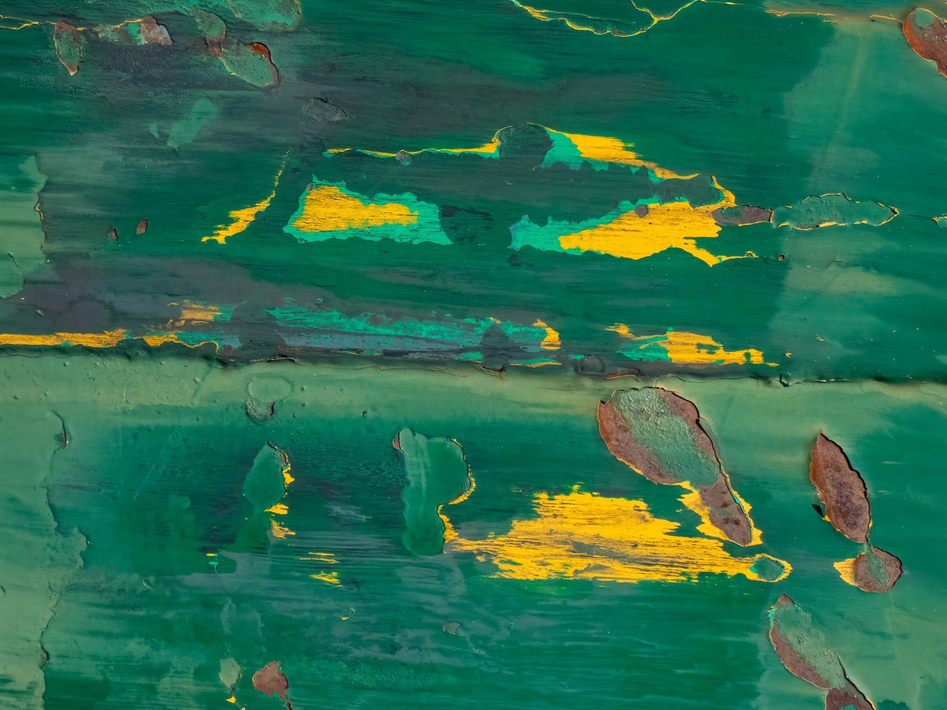 Green paint flakes away, yellow layers meet the rust, time peels back the skin