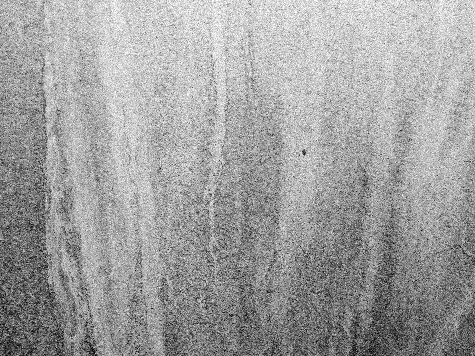 Grey wall meets the rain, dark stains run down textured stone, time leaves silent tracks