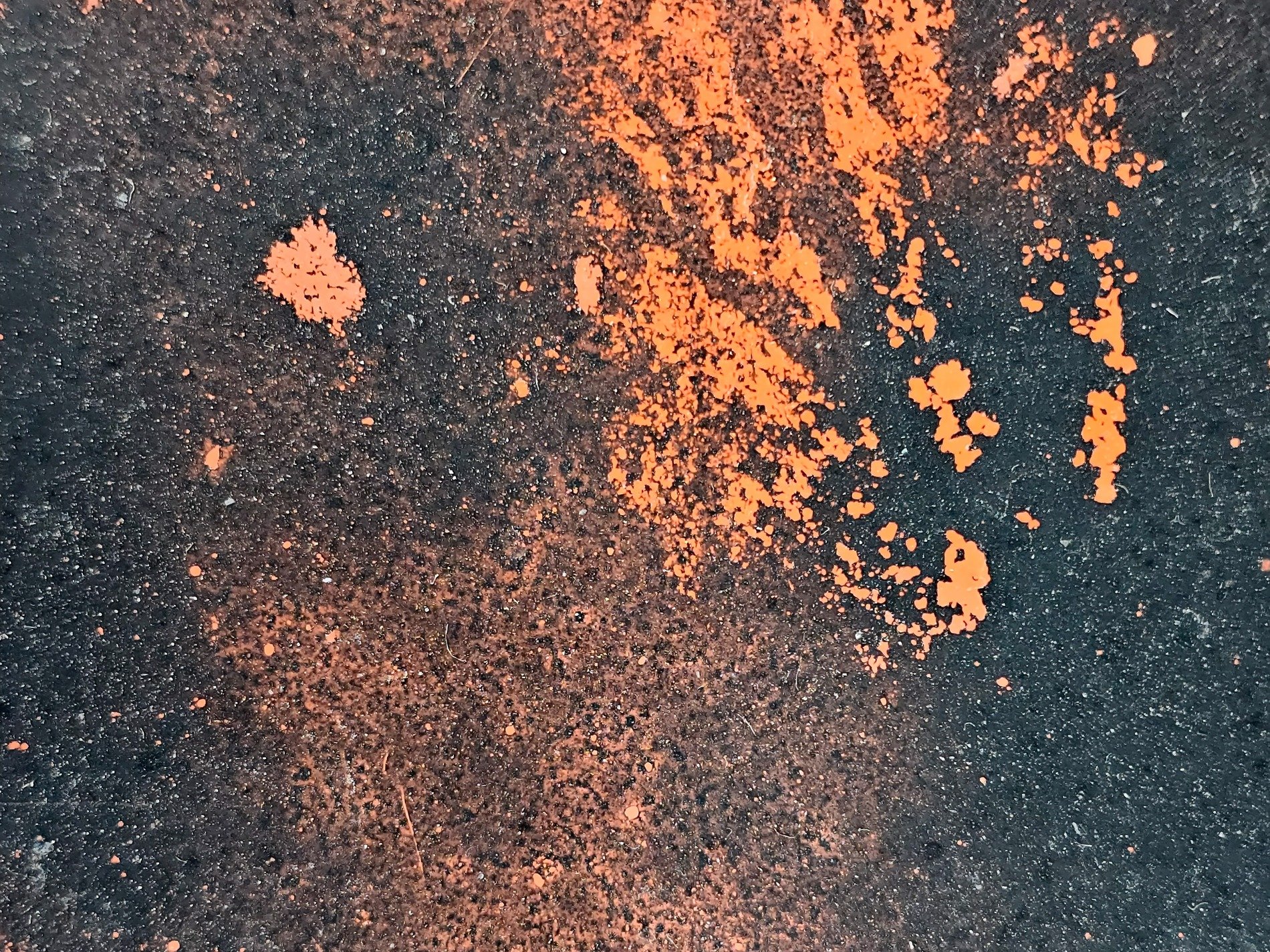 Orange dust on road, dark surface holds the bright hue, grit meets vibrant paint