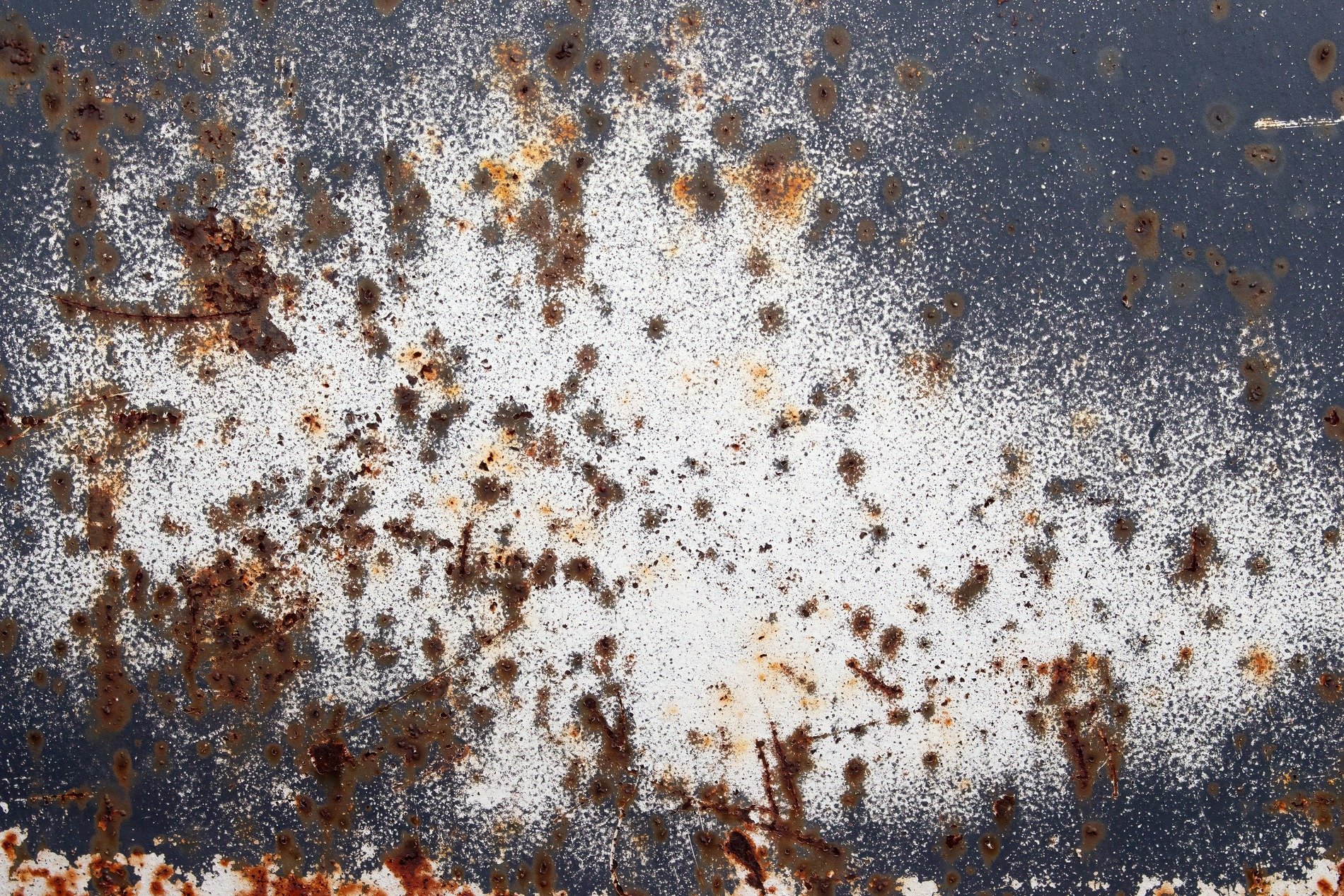 Orange rust dots bloom, white paint fades on dark metal, decay claims the steel