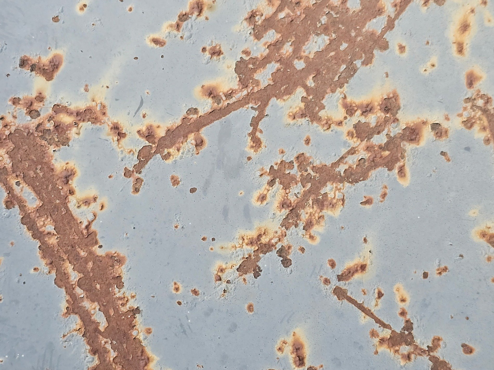 Orange rust takes hold, spreading on a faded blue, iron meets the air