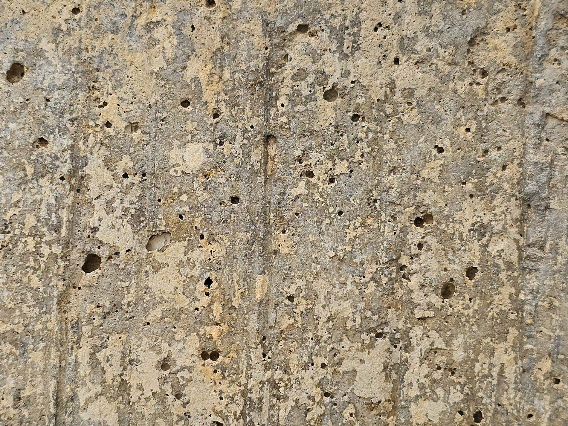 Pitted concrete wall, weathered surface wears away, shadows hide in holes